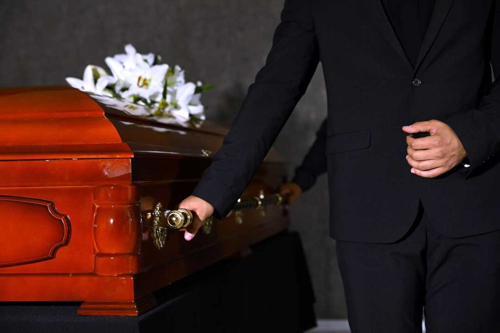 Family members review funeral documents at a table beside photographs, flowers, and a memorial service checklist.